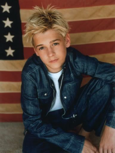 a young man sitting in front of an american flag with his hands on his knees