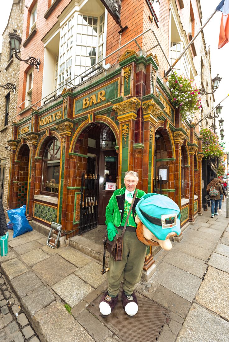 a man standing in front of a building with a bag on his shoulder and an umbrella over his head