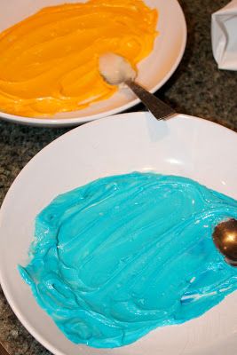 two white plates with blue and yellow frosting on them, one has a spoon in it