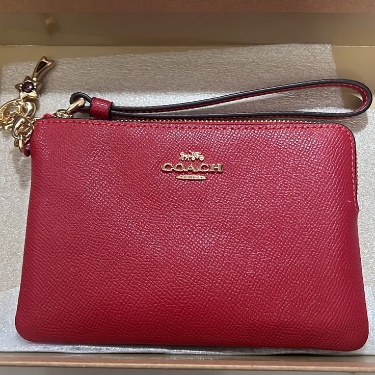 a red coach purse sitting on top of a white counter next to a box with a gold chain