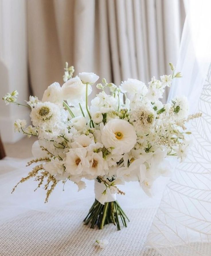 a bouquet of white flowers sitting on top of a table in front of a window