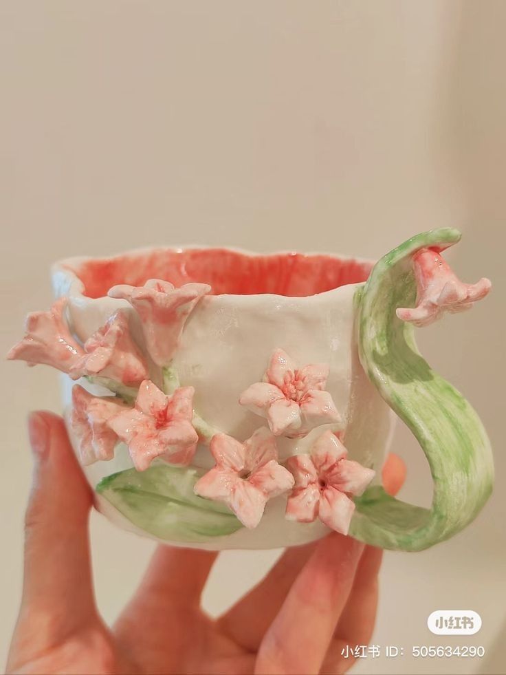 a hand holding a vase with pink flowers on it