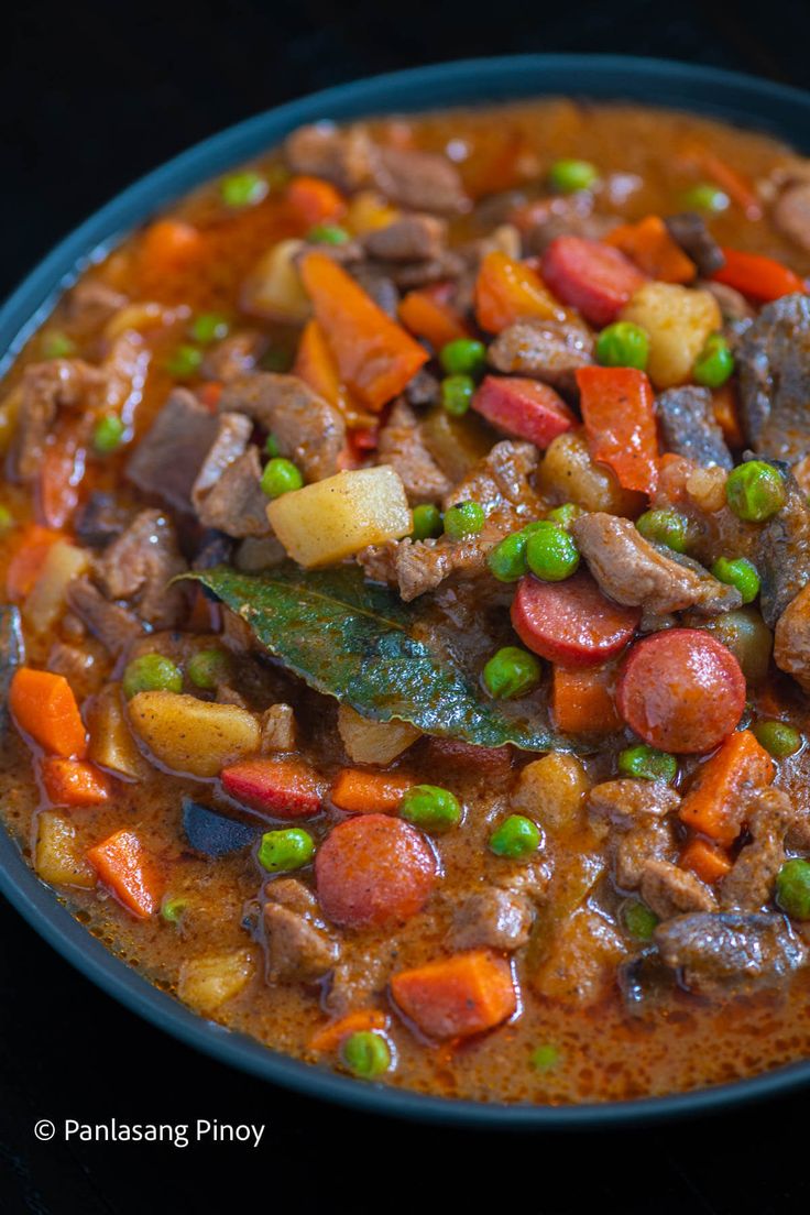 a blue bowl filled with meat and vegetables on top of a table next to a spoon