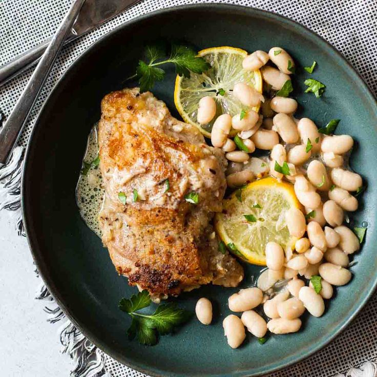 a green plate topped with meat, beans and lemons next to a fork on a table