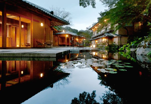 a pond in front of some buildings with lit up lights on them and lily pads floating around