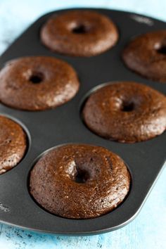 a muffin pan filled with chocolate donuts on top of a blue tablecloth