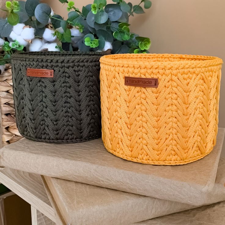 two knitted baskets sitting on top of a table next to a potted plant