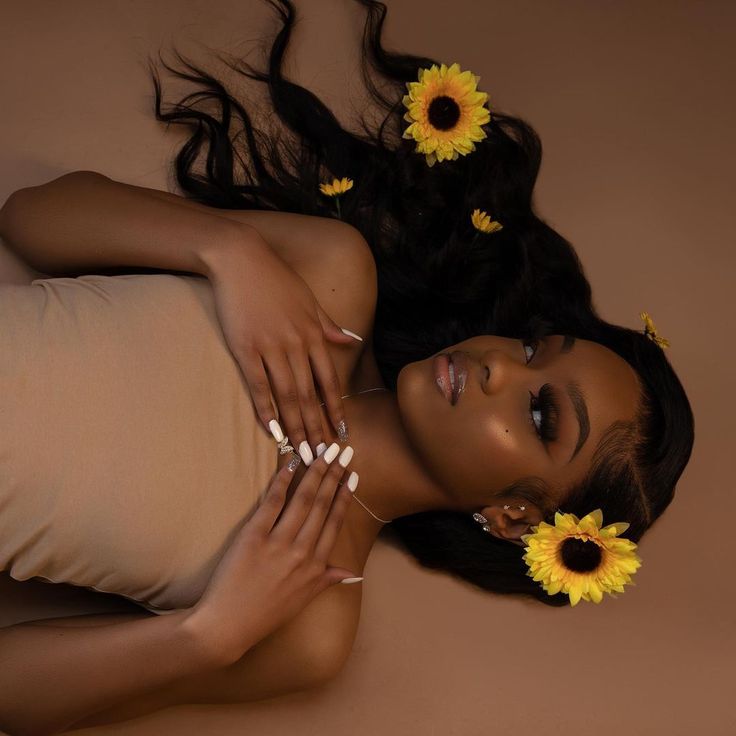 a beautiful woman laying on top of a bed with sunflowers in her hair