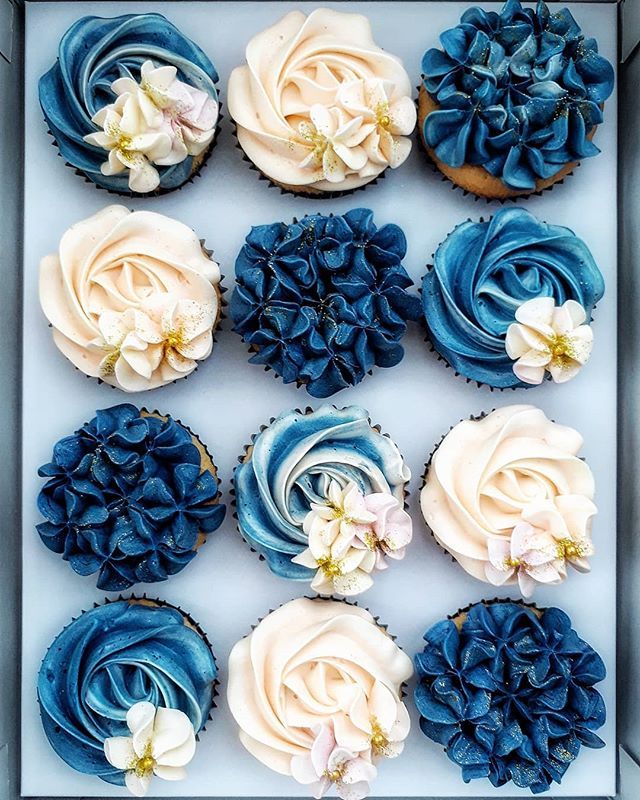 cupcakes with blue frosting and white flowers in a box