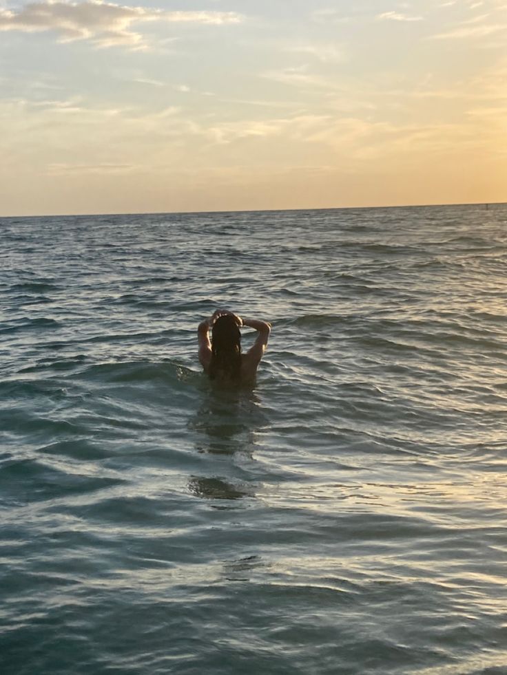 a person swimming in the ocean with their back turned to the camera and head above water