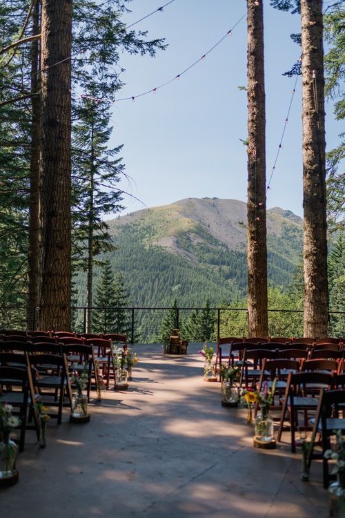 an outdoor ceremony set up with chairs and string lights in the trees, overlooking mountains