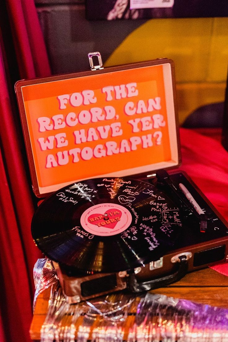 a record player sitting on top of a wooden table next to an orange sign that says for the record can we have year autograph?