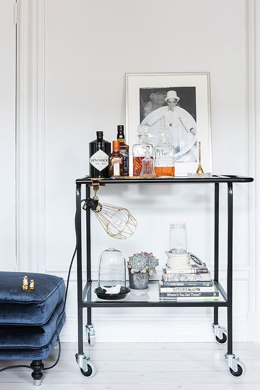 a shelf with bottles and glasses on it in front of a white wall next to a blue couch