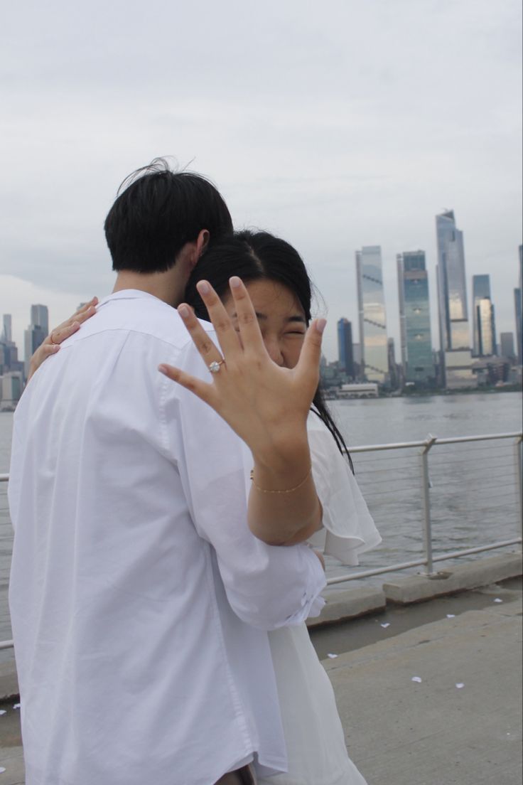 a man and woman standing next to each other in front of a body of water