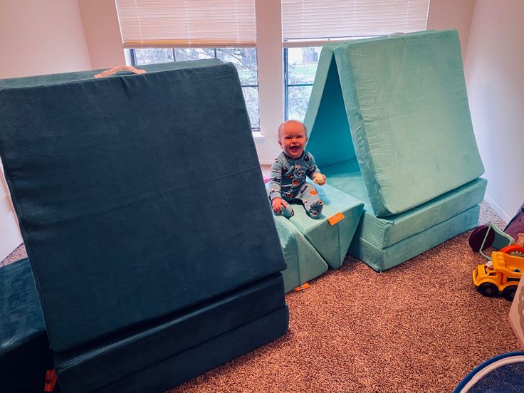 a baby sitting in a blue chair next to a giant green tent and toy cars