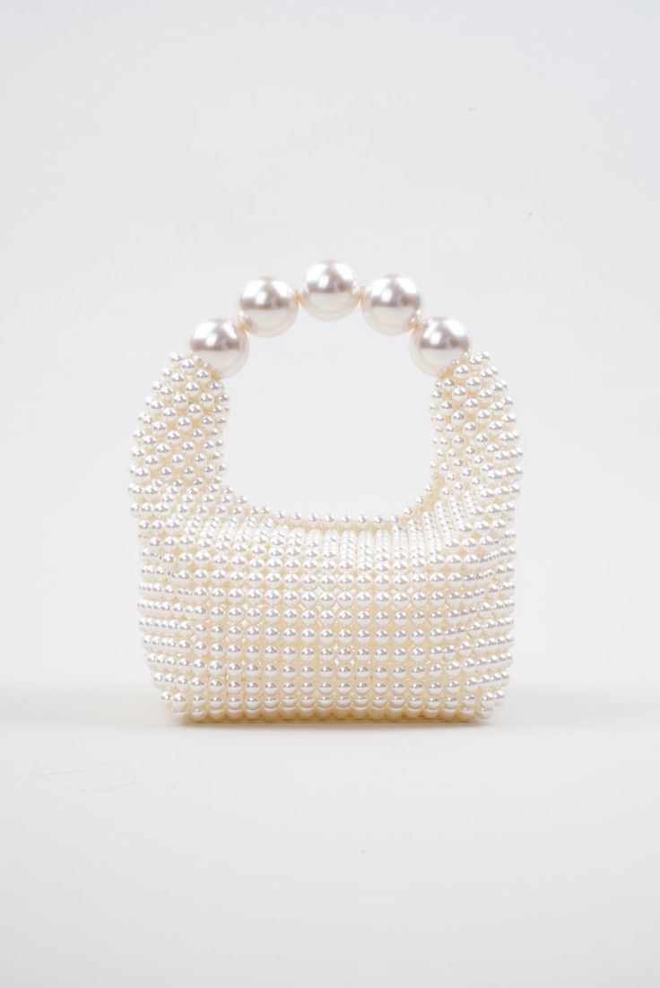 Introducing the stunning Nuit Blanche Pearl Bag by Vanina, a true embodiment of luxury and sophistication. Impossibly chic, this exquisite bag is a true masterpiece of artistry and craftsmanship that will become a wedding piece you will cherish for years to come. This bag boasts a radiant, iridescent white hue that shimmers and sparkles in the light, adding an ethereal and enchanting touch to your ensemble. Each pearl has been meticulously hand-sewn onto the bag, creating a seamless, flawless finish that exudes elegance and refinement. All of Vanina's pieces are handcrafted by skilled artisans in Lebanon, using ethically sourced and sustainable materials, making it an environmentally conscious choice you can feel good about. White All-over faux pearl embellishments Curved beaded top handle High-end White Box Bag For Gifts, Luxury Box Bag With Top Carry Handle For Party, Luxury Square Clutch With Detachable Handle, Luxury Party Box Bag With Top Carry Handle, Designer White Rectangular Evening Bag, White Top Handle Box Bag For Party, Luxury Evening Bag With Round Handle For Party, Designer Formal Evening Bag With Handle Drop, High-end Top Handle Bags For Party