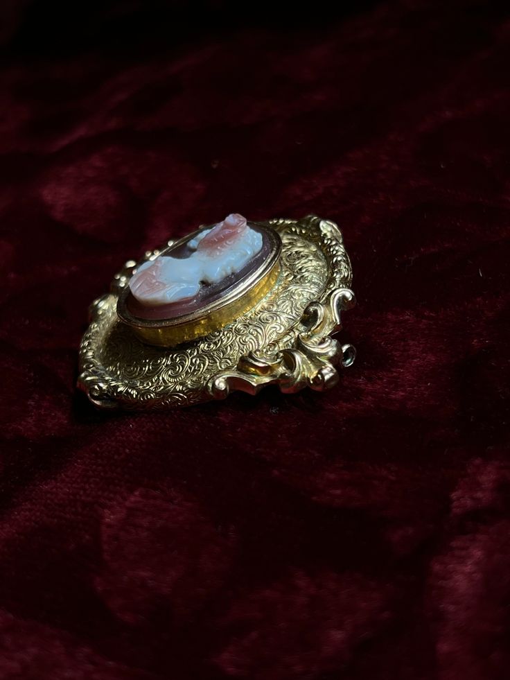 An adornment worthy of a museum! This stunning 19th century Sardonyx Cameo is a testament to Napoleon era French jewelry design. Crafted circa 1850-1860 in 18 carat gold, this brooch features a vibrant cameo of a aristocratic woman, set again a delicate peachy-hued sardonyx mount. The 18-carat gold mounting is also exceptional, with a gilded design brimming with fine detailing, and scrolling foliate motifs. The silhouette it creates makes it feel as if it should be hung in the halls of a palace! Antique Baroque Brooches With 17 Jewels, Victorian Oval Jewelry For Opera, Victorian Brooches With Locket Pendant, Victorian Locket Pendant Brooches, Victorian Style Ceremonial Yellow Gold Brooches, Antique Medallion Brooch For Wedding, Elegant Medallion Brooch For Collectors, Luxury Oval Cabochon Brooches, Antique Medallion Brooch Jewelry