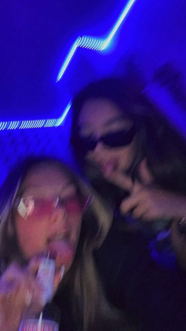 two young women are eating and drinking sodas in a bar with blue lights behind them