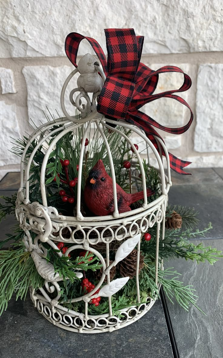 a bird in a cage decorated with pine cones and red berries is sitting on the table