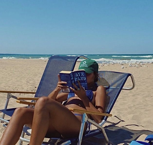 a woman reading a book while sitting in a lawn chair on the beach with her legs crossed