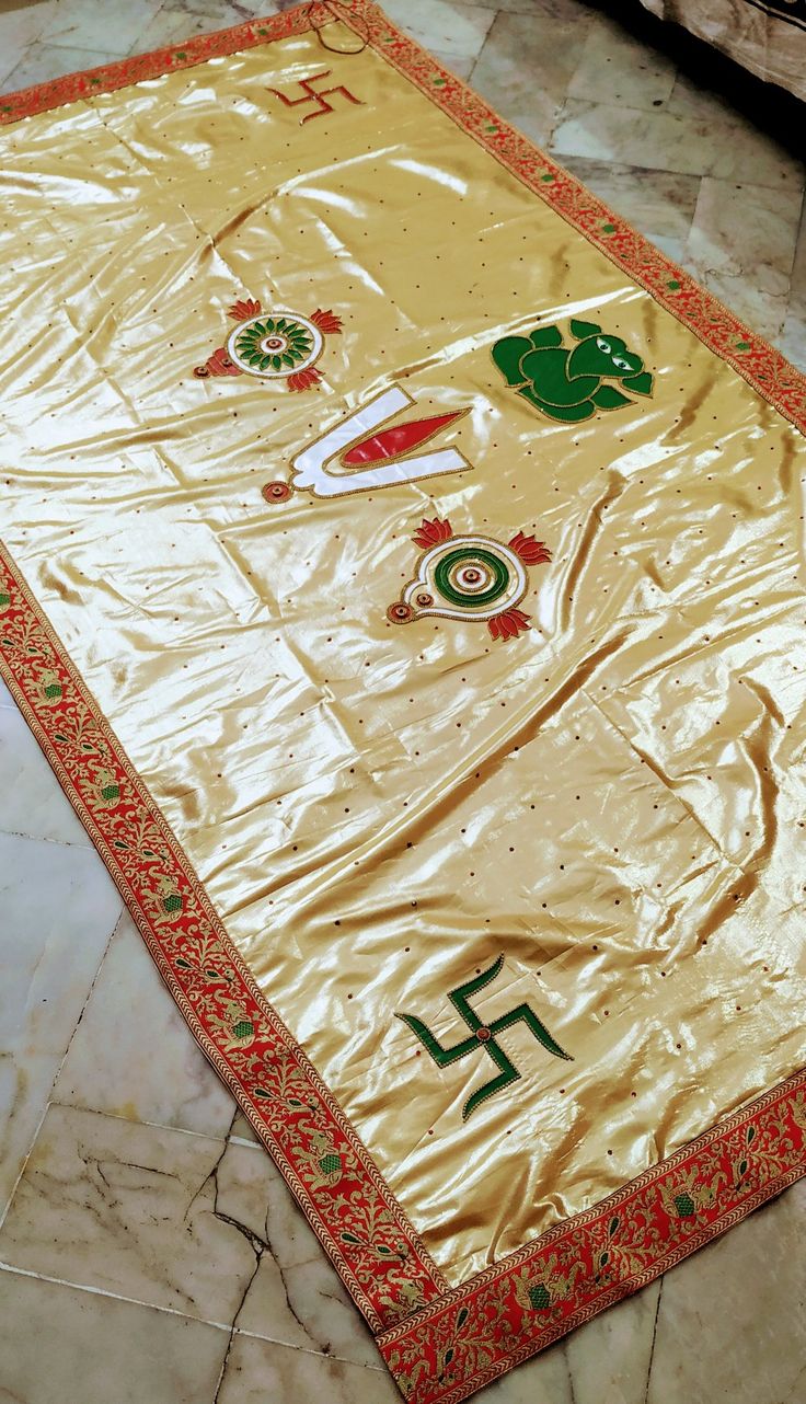 a gold table cloth with green and red designs on it, sitting on the floor