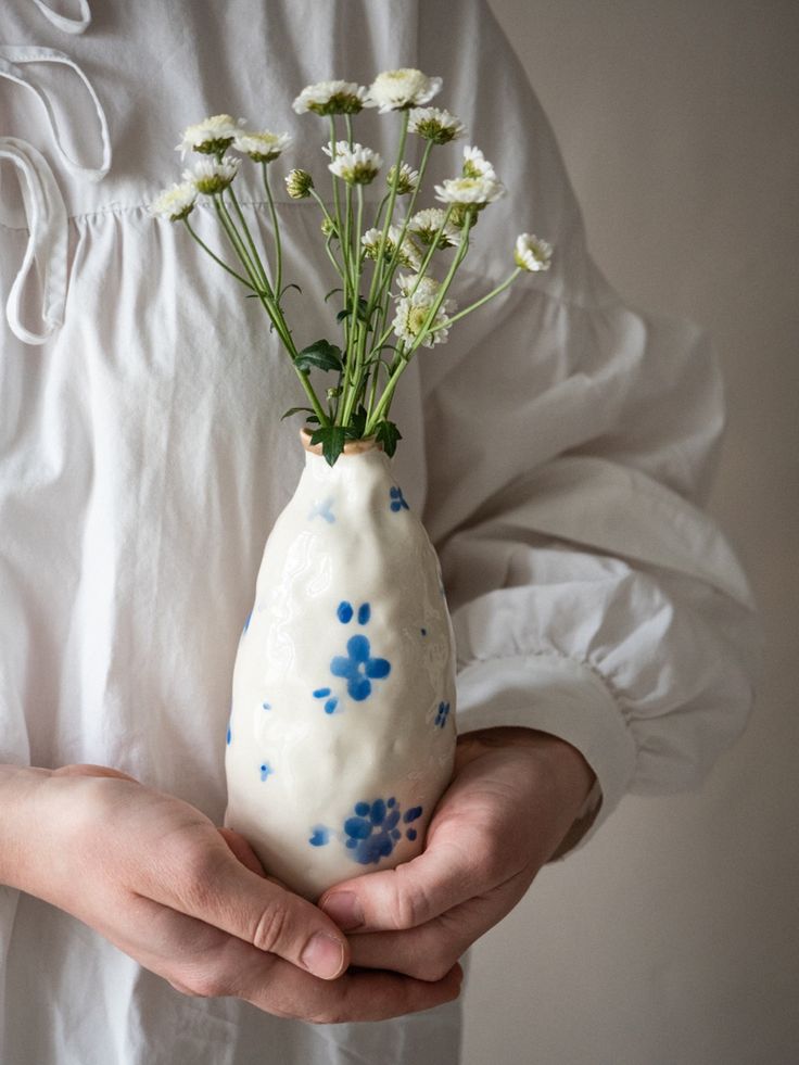 a person holding a white vase with flowers in it's hands and wearing a white shirt