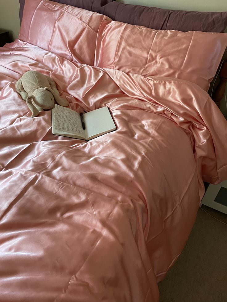 an open book and stuffed animal on a pink comforter in a bed with purple sheets