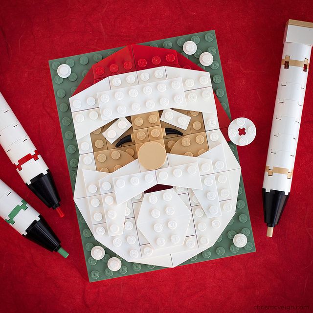 a christmas card with santa claus's face on it and three pens next to it