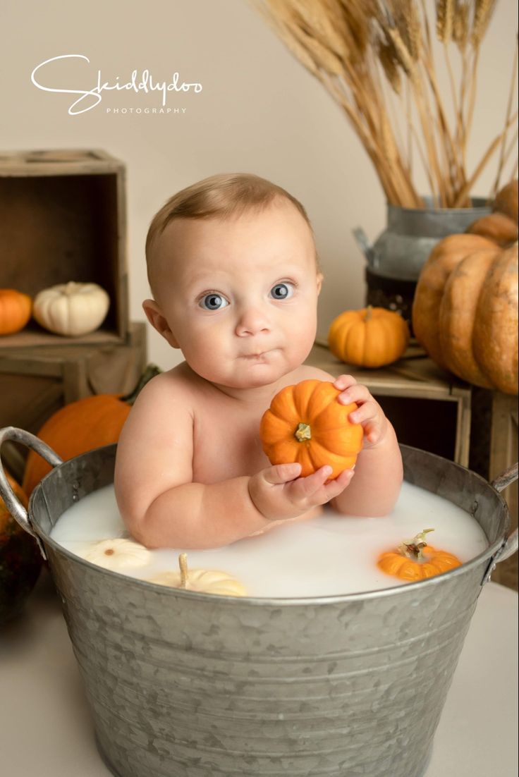 a baby is sitting in a bucket with pumpkins