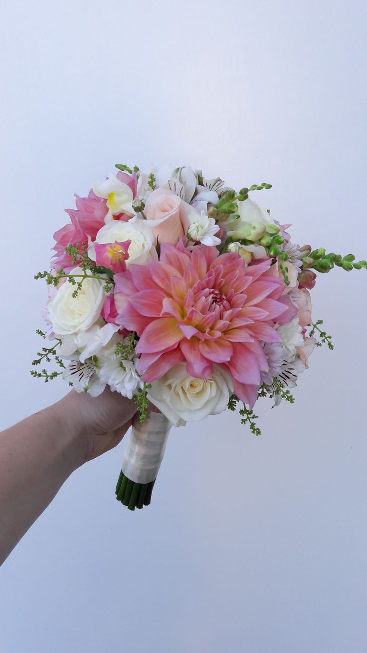 a bridal bouquet being held by someone's hand against a white background with pink and white flowers