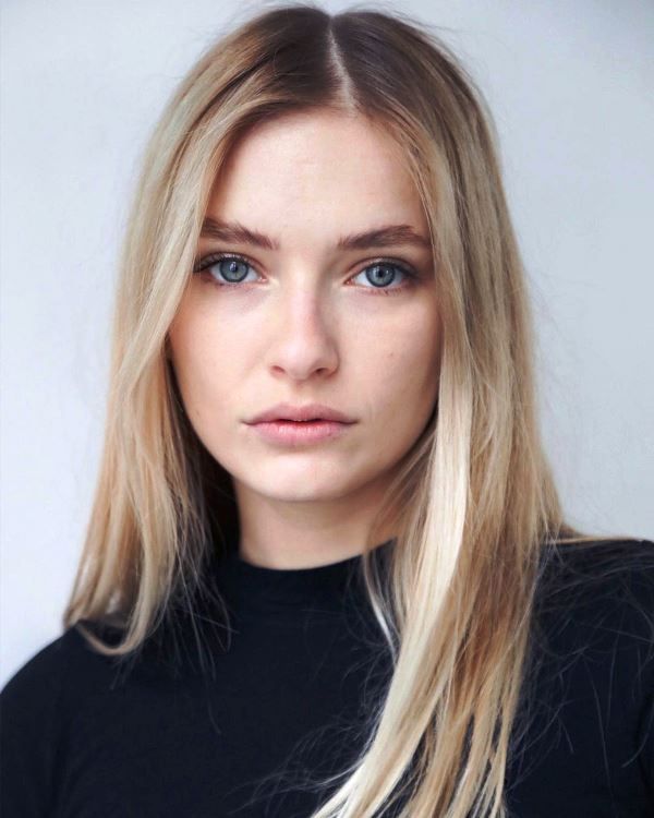 a woman with long blonde hair and blue eyes looks at the camera while wearing a black shirt