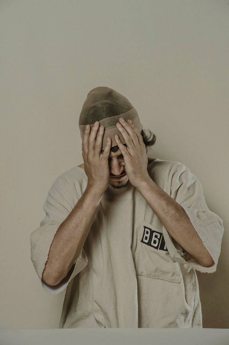 a man covering his face with both hands while standing in front of a white wall