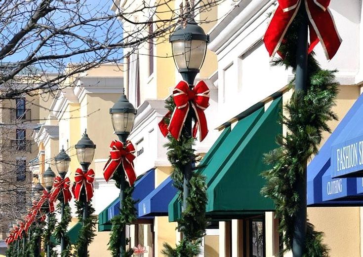 a row of street lamps decorated with red bows and christmas garlands on the sidewalk