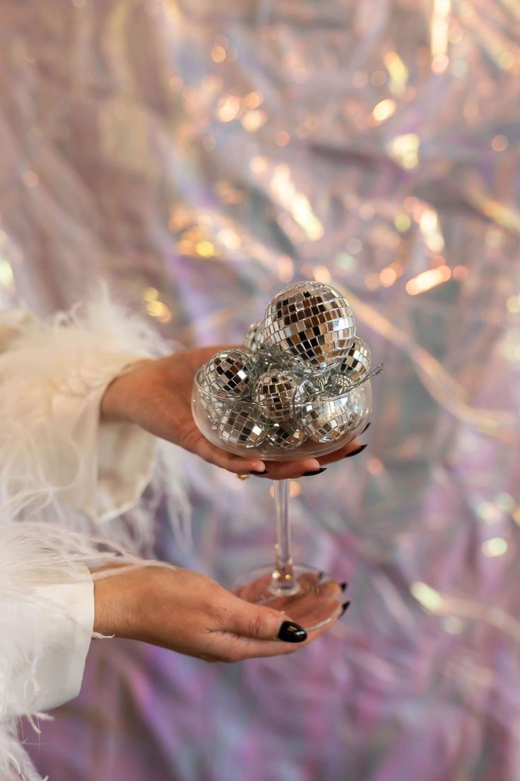 a woman holding a wine glass in front of a disco ball wallpapered backdrop