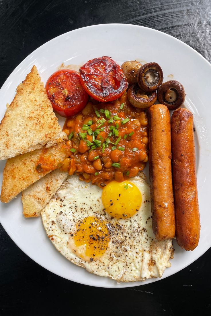 a white plate topped with eggs, sausages and beans next to toasted bread