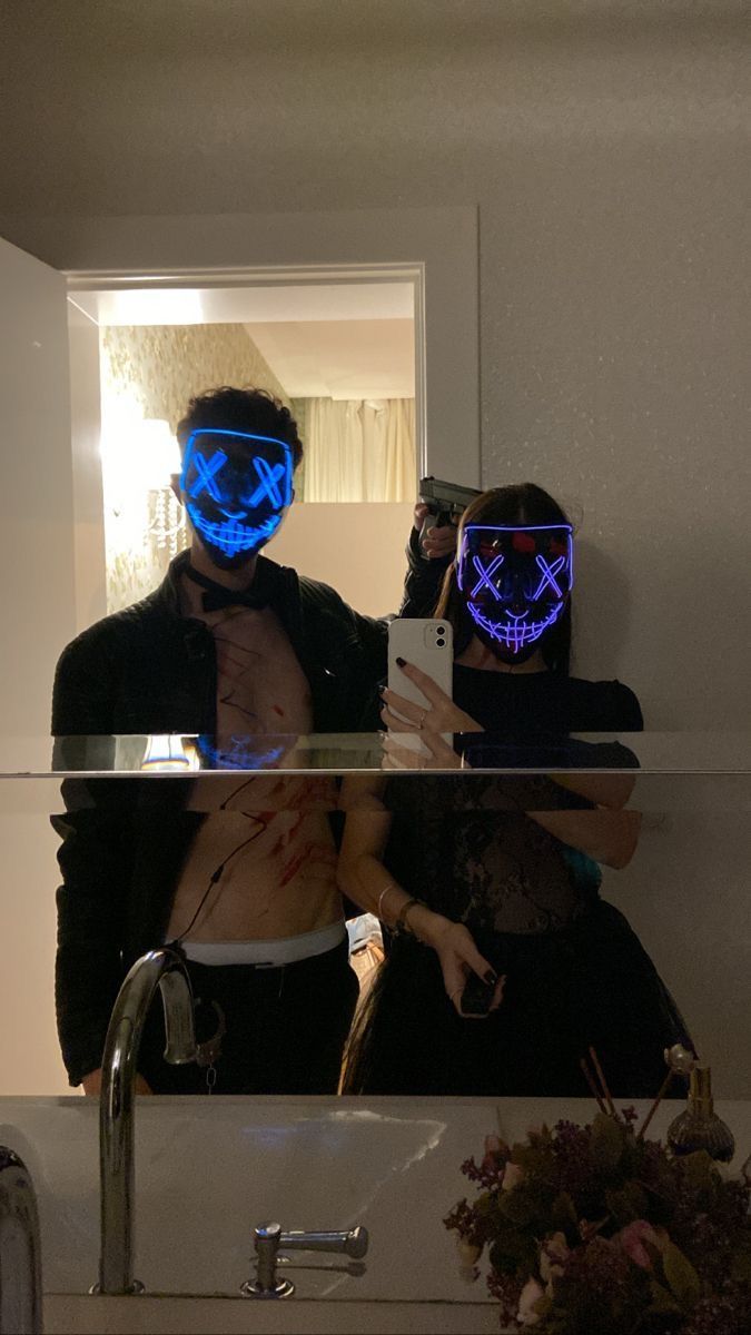 two people wearing neon masks are taking a selfie in front of a bathroom mirror