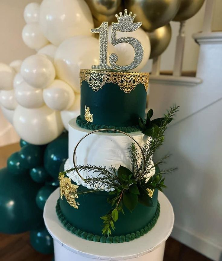 a three tiered green and gold wedding cake with white frosting, greenery and a crown on top