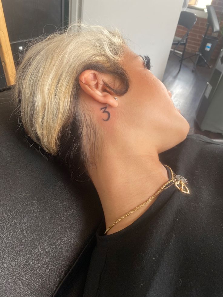 a woman with blonde hair has a small tattoo on her neck and behind her ear