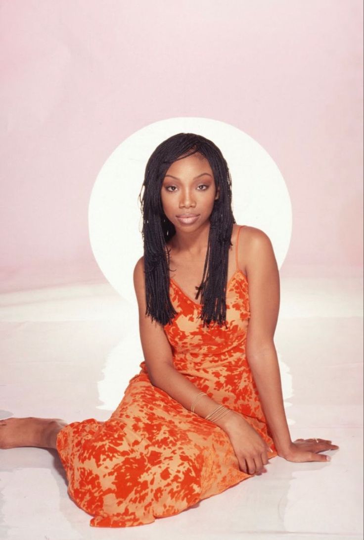 a woman in an orange dress sitting on the floor with her legs crossed and eyes closed