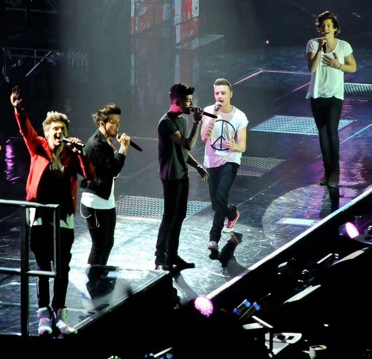 group of people standing on stage with microphones in their hands and one person holding up his hand