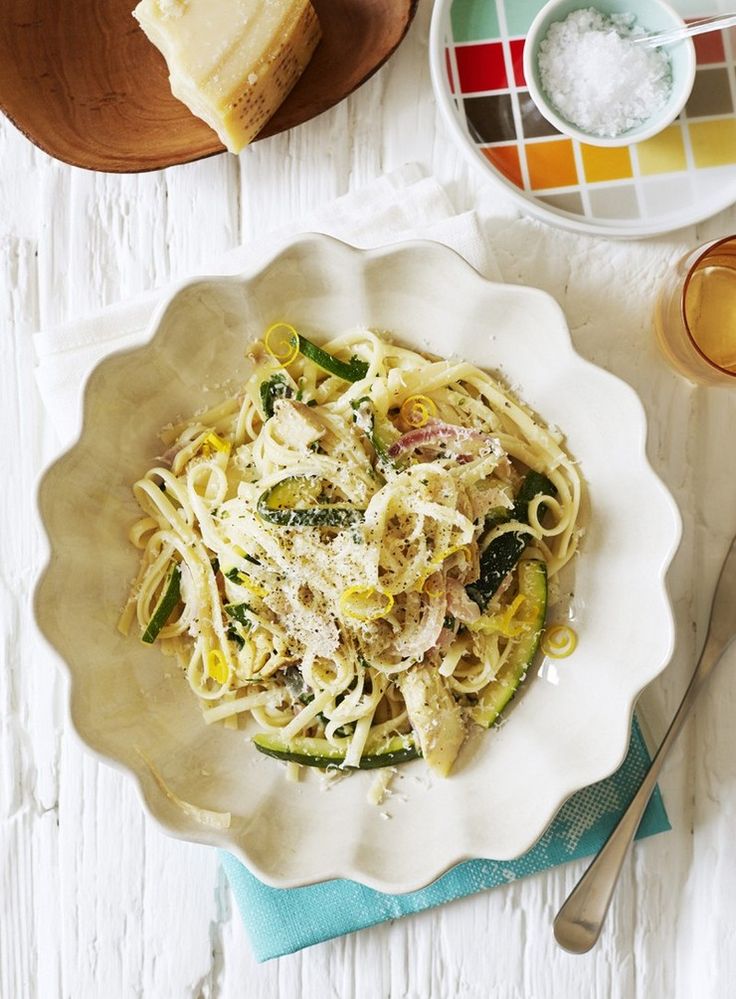 a plate of pasta and bread on a white wooden table with utensils next to it