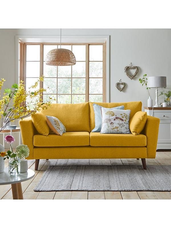 a living room with yellow couches and flowers in vases on the coffee table