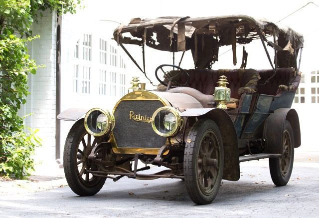 an old fashioned car is parked in front of a white building with ivy growing around it