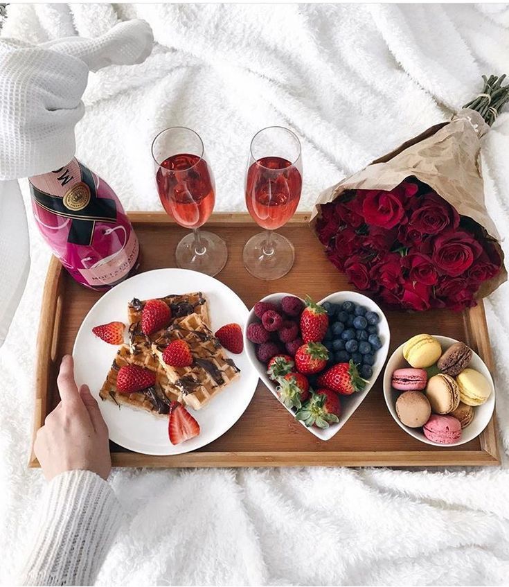 a tray filled with food and wine on top of a bed next to two glasses of wine