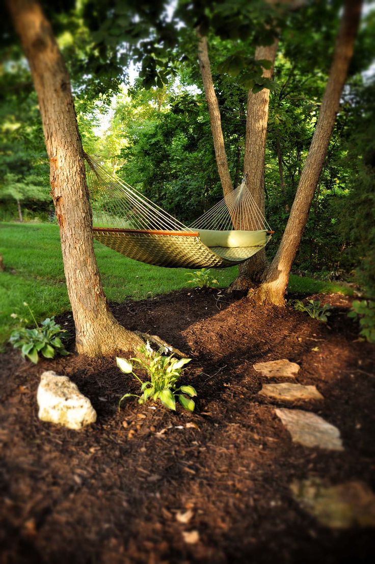 a hammock hanging between two trees in a park with rocks and dirt on the ground