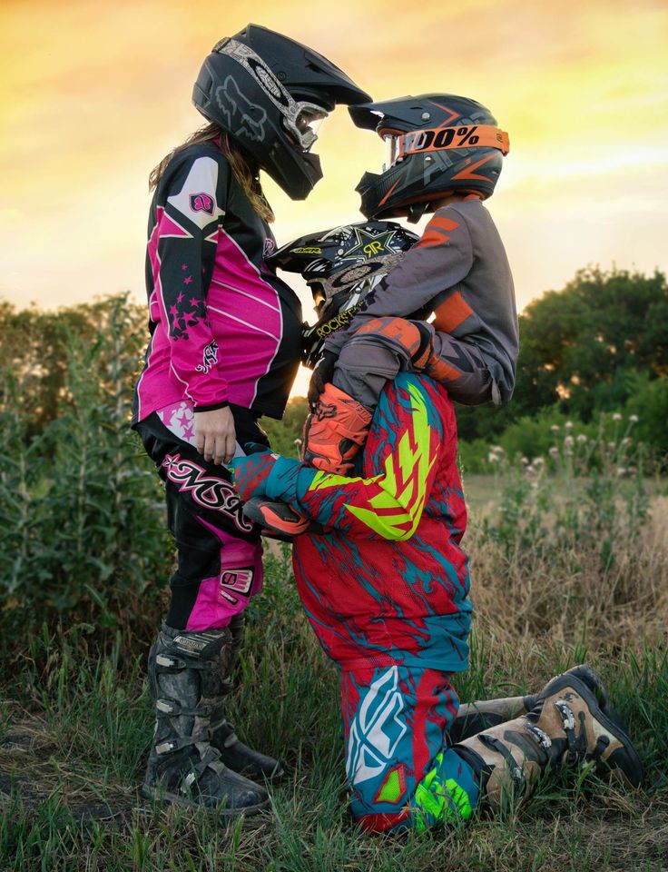 two young children wearing helmets and knee pads standing next to each other in the grass