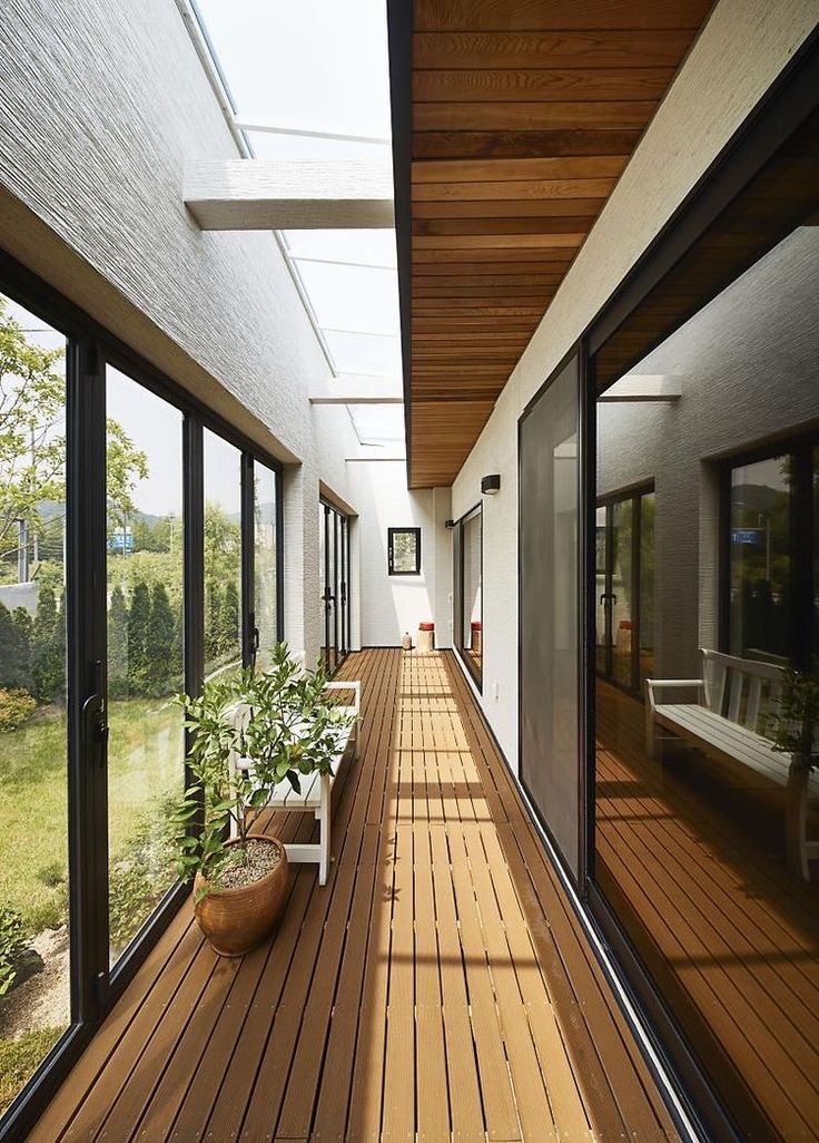 a long wooden deck with potted plants on the side and large glass doors leading to another room