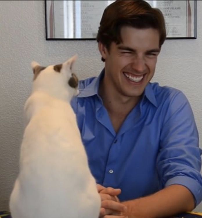 a man sitting at a table with a white cat in front of him and smiling