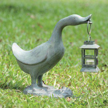 a bird statue holding a lantern in its beak on top of a green grass covered field