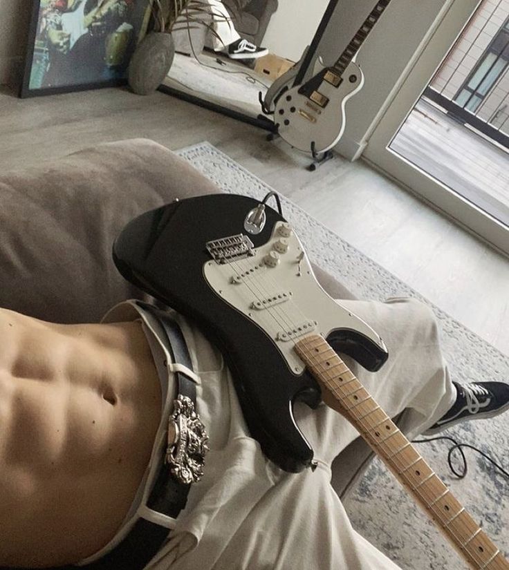 a man laying on top of a couch with a guitar strapped to his chest next to him